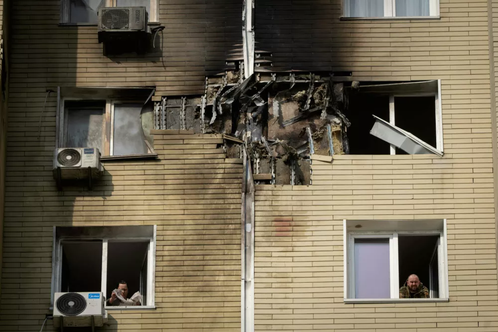 A resident watches as his neighbour cleans up the damaged apartment in a multi-storey house after a Russia's night drone attack in Kyiv, Ukraine, Sunday, March 23, 2025. (AP Photo/Efrem Lukatsky)