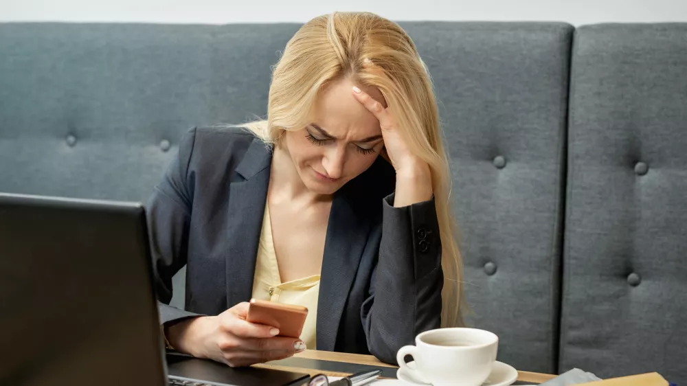 Dissatisfied surprised caucasian young woman look at smartphone screen in the home office. / Foto: Okskukuruza