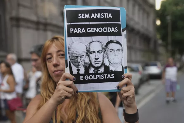 A demonstrator holds a poster featuring President Donald Trump, from left, Israel's Prime Minister Benjamin Netanyahu and Brazil's former President Jair Bolsonaro, with a message that reads in Portuguese; "No amnesty for genociders and coup plotters" during a march marking the anniversary of the 1964 military coup, in Rio de Janeiro, Tuesday, April 1, 2025. (AP Photo/Silvia Izquierdo)