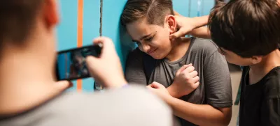 A young boy is being bullied by peers at school. The boy is upset as another boy grabs his neck. A third boy records the bullying incident on his phone. Bullying of teenager in high scool. / Foto: Rawpixel