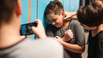 A young boy is being bullied by peers at school. The boy is upset as another boy grabs his neck. A third boy records the bullying incident on his phone. Bullying of teenager in high scool. / Foto: Rawpixel