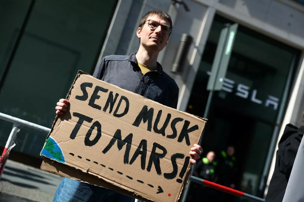 A person holds a placard during a protest outside a Tesla showroom at Mall of Berlin under the slogan "#TeslaTakedown" against Tesla and its CEO Elon Musk and against what organisers say is the destruction of democracy and the climate by the rich, in Berlin, Germany, April 5, 2025. REUTERS/Christian Mang