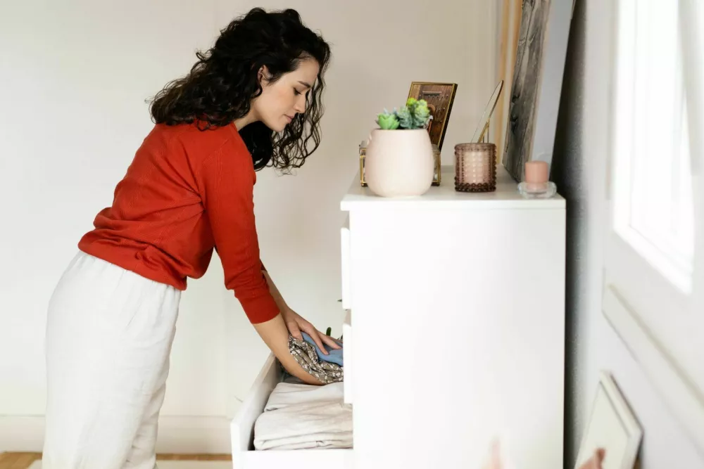 Young woman in red seawter storing and tidying clothes in the drawers at home / Foto: Asife