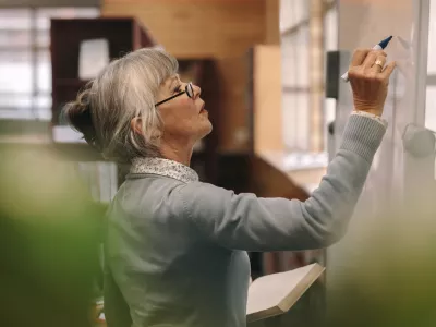 Side view of a senior female teacher writing on a white board in classroom. Close up of a woman lecturer teaching in classroom. / Foto: Jacoblund