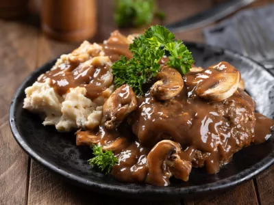 Salisbury steak with mushroom gravy garnished with parsley and mashed potatoes on a black plate / Foto: Chas53