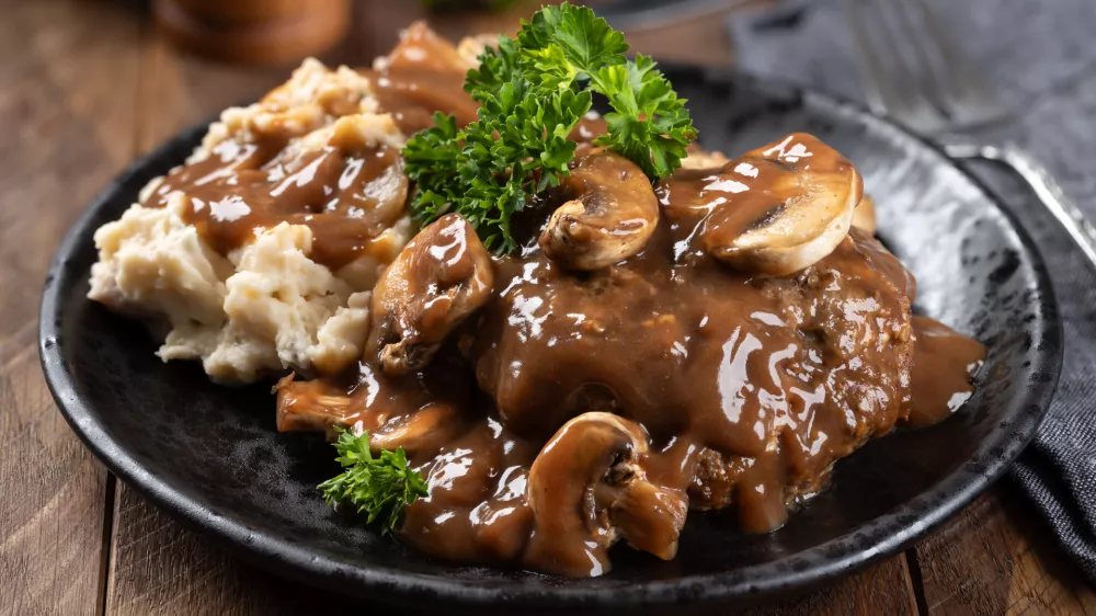 Salisbury steak with mushroom gravy garnished with parsley and mashed potatoes on a black plate / Foto: Chas53