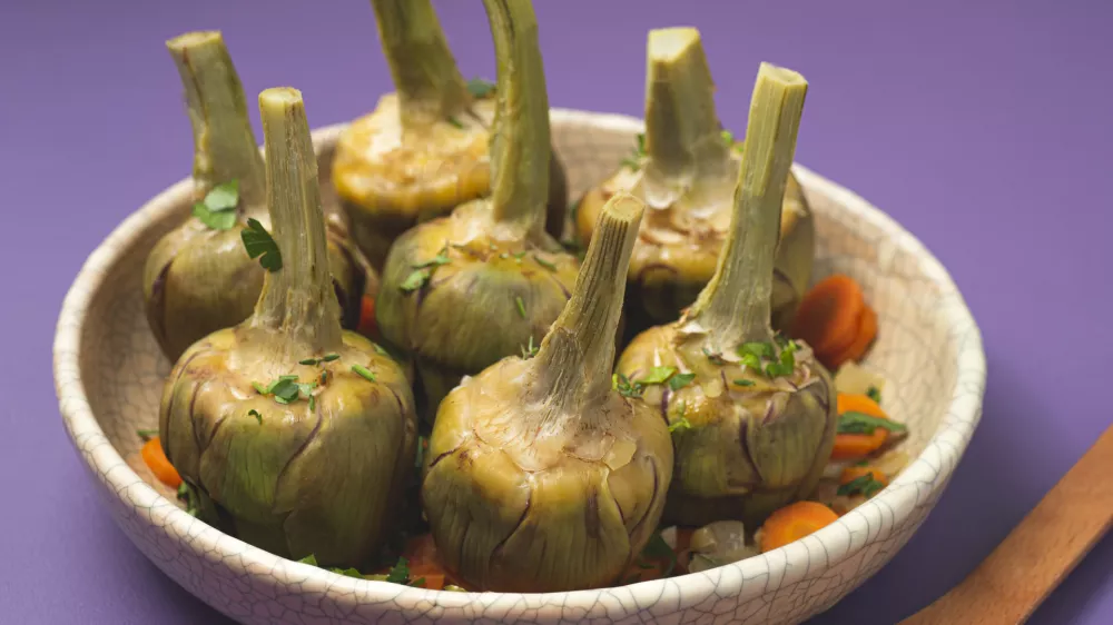 French artichokes &agrave; la Barigoule or Carciofi alla provenzal. Provencal artichokes stewed with carrots, onions, white wine, bay leaves and Proven&ccedil;al herbs. Spring recipes from southern France. Lavender background / Foto: Uliu