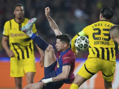 Barcelona's Robert Lewandowski, center, attempts a shot at goal in front of Dortmund's Emre Can during the Champions League quarterfinal first leg soccer match between Barcelona and Borussia Dortmund, at the Lluis Companys Olympic stadium in Barcelona, Spain, Wednesday, April 9, 2025. (AP Photo/Emilio Morenatti)