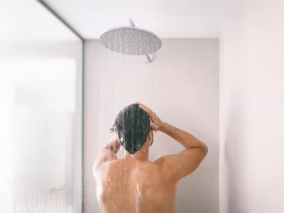 Man taking a shower washing hair with shampoo product under water falling from luxury rain shower head. Morning routine luxury hotel lifestyle guy showering. body care hygiene.