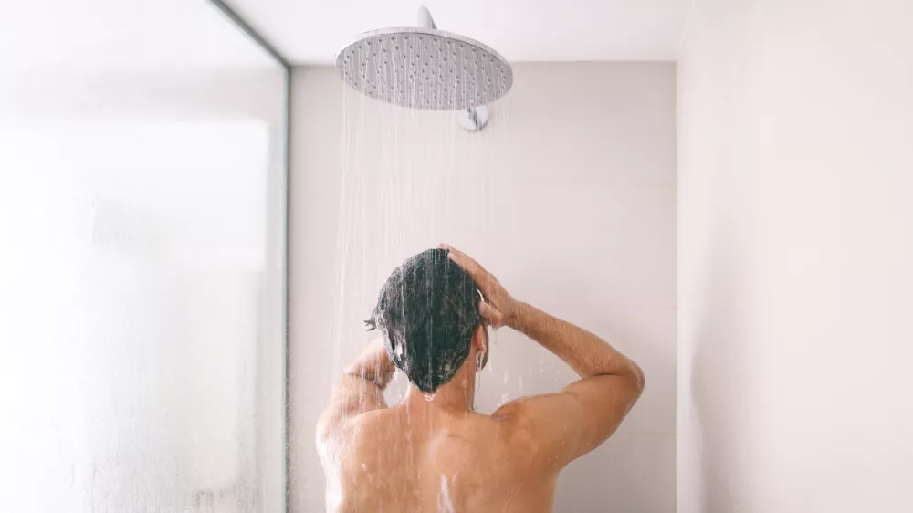 Man taking a shower washing hair with shampoo product under water falling from luxury rain shower head. Morning routine luxury hotel lifestyle guy showering. body care hygiene.