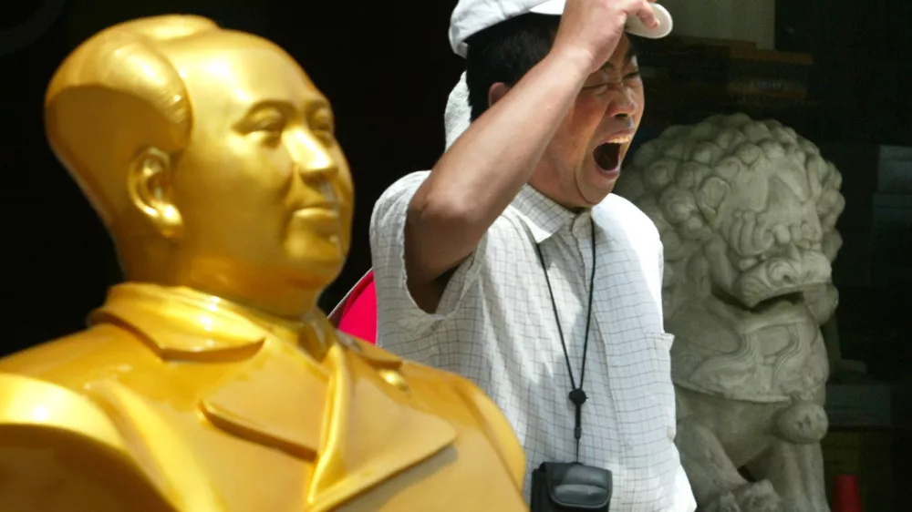 A Chinese tourist yawns as he walks past a bust of Mao Zedong and a stone lion along a commercial district in Beijing, China, Sunday, June 29, 2003. Domestic tourism is trickling back into the Chinese capital after the WHO travel advisory was lifted. The city's tourist industry - which accounts for about one-third of its economic output - lost an estimated 45 billion yuan (US$5.4 billion) in tourism dollars due to the SARS epidemic as domestic and foreign tourists kept away. (AP Photo/Ng Han Guan)