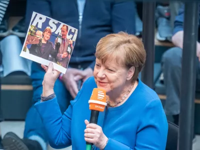 10 April 2025, Berlin: Former German Chancellor Angela Merkel holds a picture of her and Friedrich Merz as she speaks during her appearance as a guest on Deutschlandfunk's live radio show "Studio 9" at the Humboldt Forum. Photo: Michael Kappeler/dpa