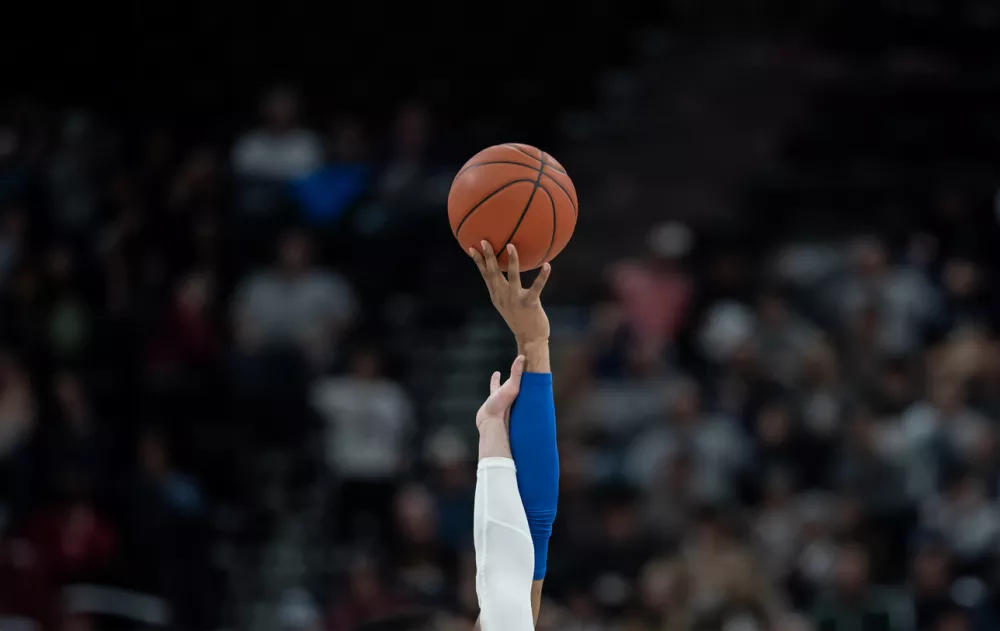 Two people reaching for the basketball at the opening tipoff of a basketball game. / Foto: Yobro10