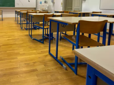 Modern, well-lit classroom with rows of empty wooden desks and blue-framed chairs on a polished wooden floor. The organized, quiet setting evokes themes of education, back to school, academic preparation, and the learning environment. Perfect for content related to schools, teaching, or educational systems. / Foto: Bamm-bamm