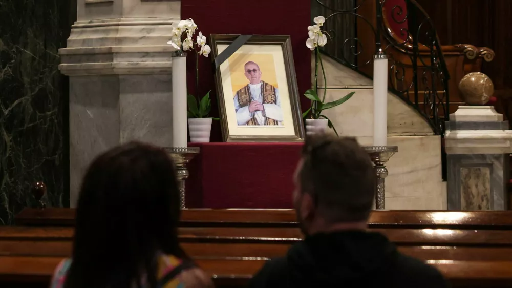 A couple sits near a portrait of Pope Francis, following his death, in the Catholic Cathedral of Saint Dionysius the Areopagite, in Athens, Greece, April 22, 2025. REUTERS/Louisa Gouliamaki