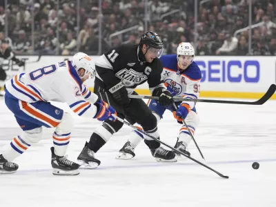 Los Angeles Kings center Anze Kopitar, center, moves the puck while under pressure from Edmonton Oilers right wing Connor Brown, left, and center Ryan Nugent-Hopkins during the second period in Game 1 of an NHL hockey first-round playoff series Monday, April 21, 2025, in Los Angeles. (AP Photo/Mark J. Terrill)