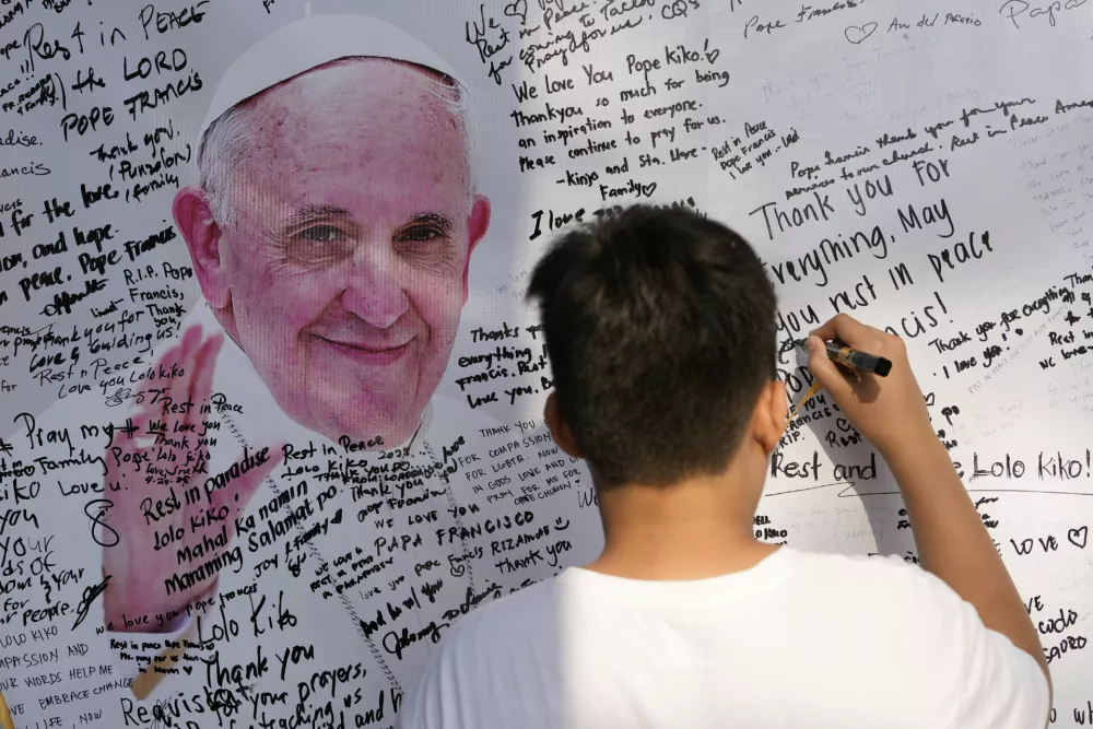 A Catholic devotee writes on a message board for the late Pope Francis outside the St. Peter Parish in Quezon city, Philippines Thursday, April 24, 2025. (AP Photo/Aaron Favila)