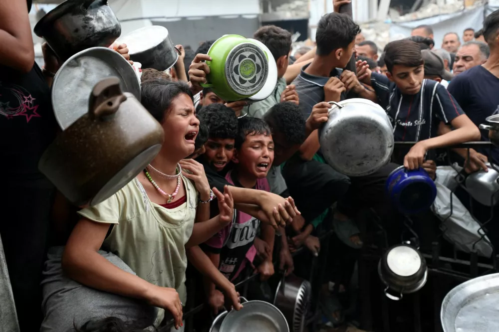 Children react as Palestinians wait to receive food cooked by a charity kitchen, in Beit Lahia, northern Gaza Strip, April 24, 2025. REUTERS/Mahmoud Issa