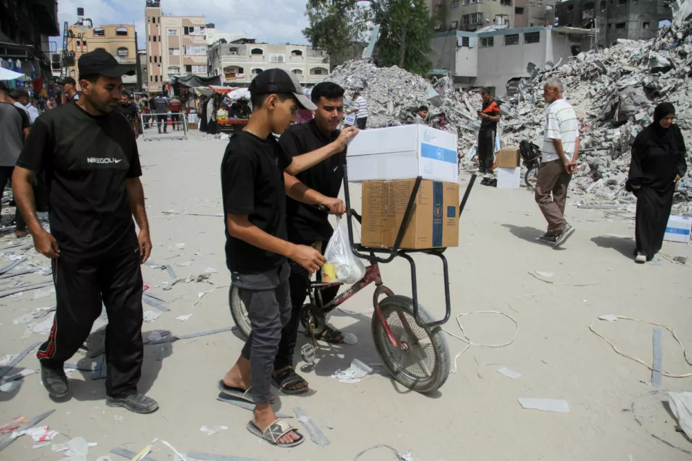 FILE PHOTO: People load boxes on a bike, as Palestinians gather to receive aid, including food supplies provided by World Food Program (WFP), outside a United Nations distribution center, amid the Israel-Hamas conflict, in Jabalia in the northern Gaza Strip, August 24, 2024. REUTERS/Mahmoud Issa/File Photo