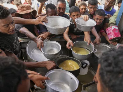 Palestinians struggle to receive cooked food distributed at a community kitchen in Khan Younis, southern Gaza Strip, Wednesday, May 14, 2025. (AP Photo/Abdel Kareem Hana)
