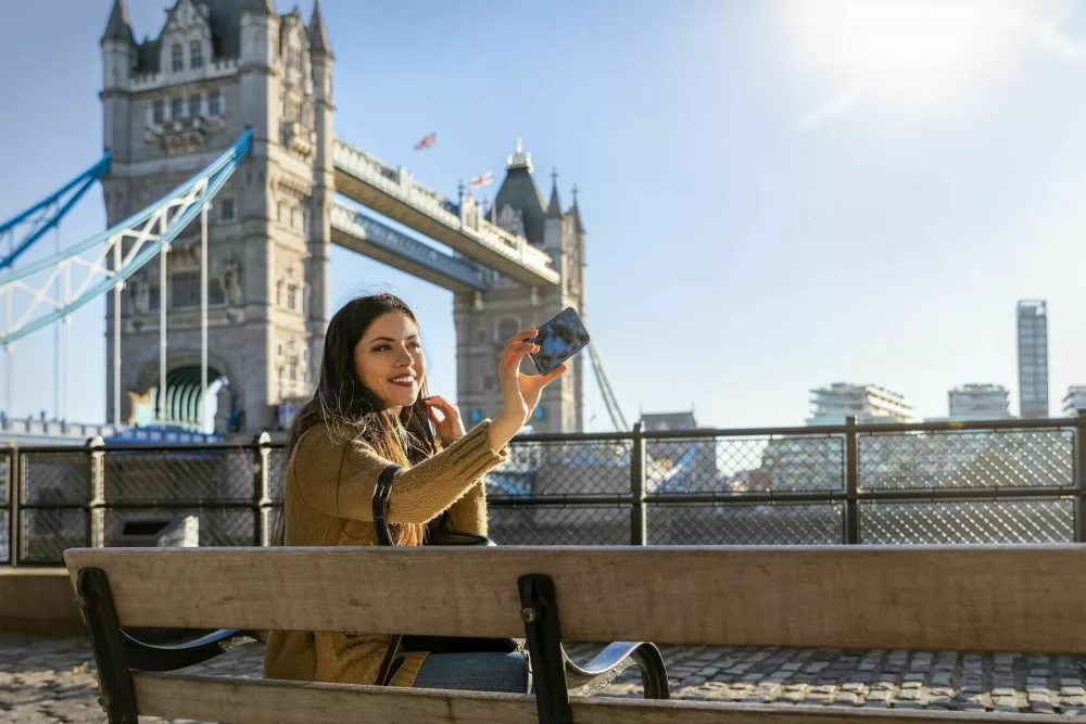 Beautiful female London traveler takes a selfie picture with her phone in front of the Tower Bridge on a sunny day / Foto: Shansche