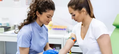 Preparation for blood test with pretty young woman by female doctor medical uniform on the table in white bright room. Nurse pierces the patient's arm vein with needle blank tube. / Foto: Stefanamer