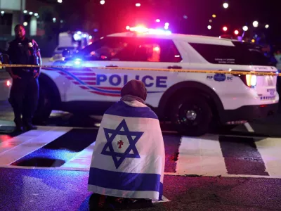 A man, with an Israeli flag with a cross in the center, kneels next to emergency personnel working at the site where, according to the U.S. Homeland Security Secretary, two Israeli embassy staff were shot dead near the Capital Jewish Museum in Washington, D.C., U.S. May 21, 2025. REUTERS/Jonathan Ernst  TPX IMAGES OF THE DAY