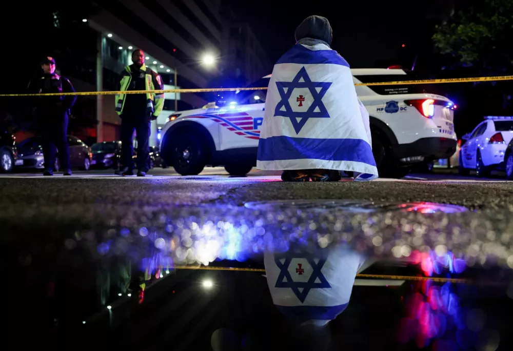 A man, with an Israeli flag with a cross in the center, looks on next to police officers working at the site where, according to the U.S. Homeland Security Secretary, two Israeli embassy staff were shot dead near the Capital Jewish Museum in Washington, D.C., U.S. May 21, 2025. REUTERS/Jonathan Ernst