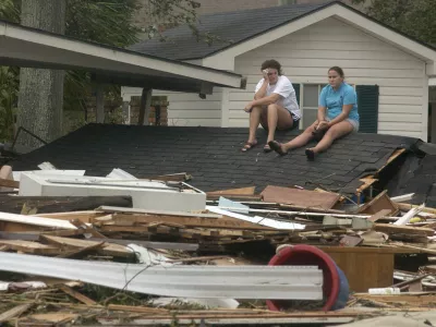 Melanie Seaman, left, and her daughter Miranda sit on the detached roof of a relatives home on Washington Avenue in Pascagoula, Miss., on Monday, Aug. 29, 2005, after Hurricane Katrina made landfall causing severe damage to the area. (AP Photo/Mississippi Press, William Colgin)