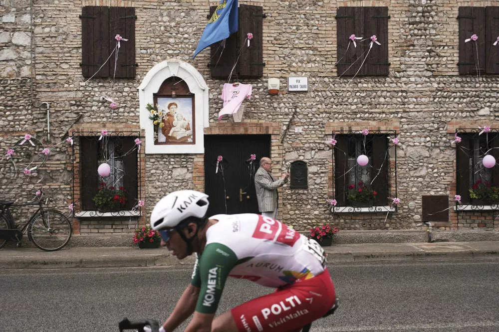 Pink balloons hang from a building's windows as the pack rides past during the 14th stage of the Giro d'Italia cycling race from Treviso to Nova Gorica/Gorizia, Italy, Saturday, May 24, 2025. (Marco Alpozzi/LaPresse via AP)
