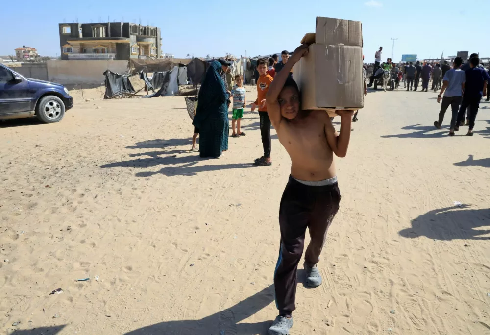 A youngster carries a box as Palestinians seeking aid gather near an aid distribution site run by the U.S.-backed Gaza Humanitarian Foundation, in Rafah, in the southern Gaza Strip, May 27, 2025. REUTERS/Hatem Khaled