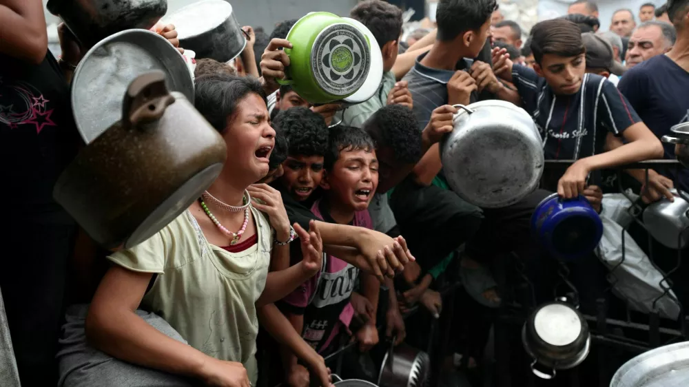 Children react as Palestinians wait to receive food cooked by a charity kitchen, in Beit Lahia, northern Gaza Strip, April 24, 2025. REUTERS/Mahmoud Issa