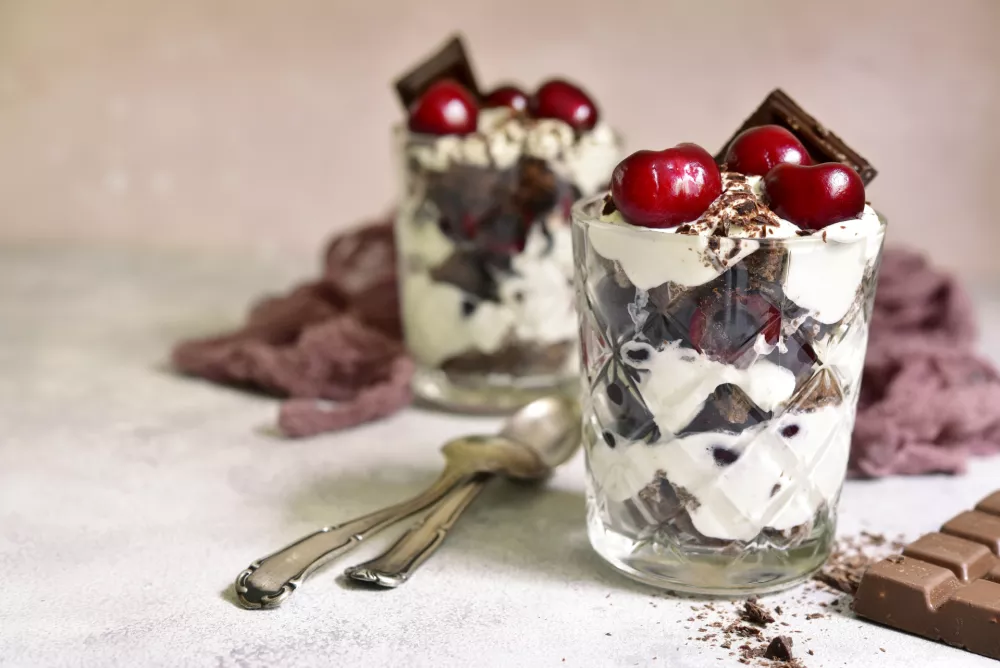 Layered dessert "Black forest" - chocolate biscuit,whipped cream, cherry and rum or brendy in a glasses over light slate, stone or concrete background. / Foto: Lilechka75