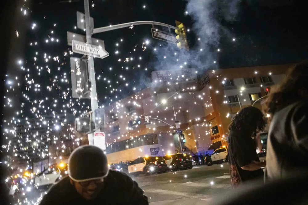 People take cover as a fire work explodes during a protest near the Metropolitan Detention Center in downtown Los Angeles, Sunday, June 8, 2025. (AP Photo/Ethan Swope)