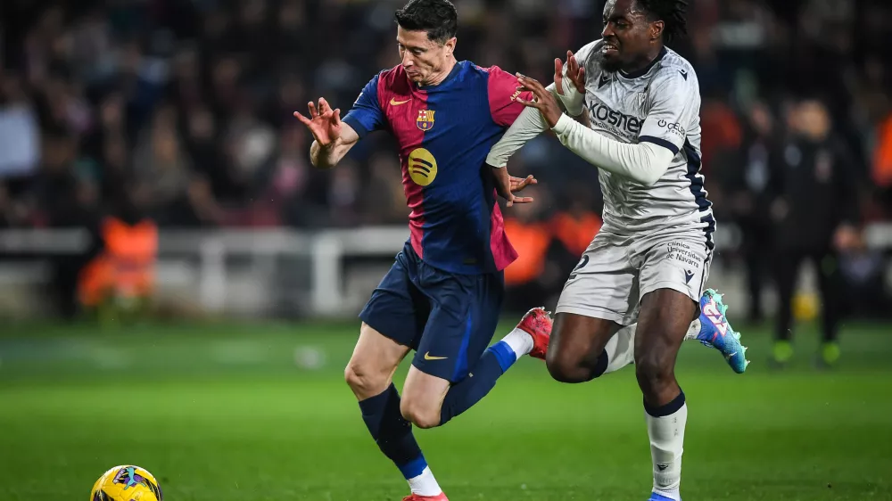 27 March 2025, Spain, Barcelona: Barcelona's Robert Lewandowski and Osasuna's Enzo Boyomo battle for the ball during the Spanish La Liga soccer match between Real Madrid and CA Osasuna at Estadi Olimpic Lluis Companys. Photo: Matthieu Mirville/ZUMA Press Wire/dpa