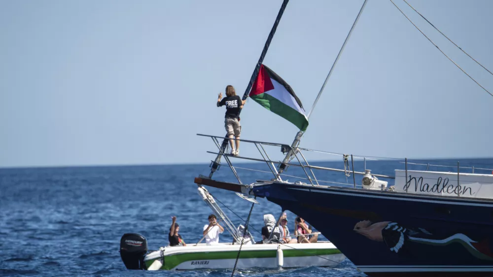 Climate activist Greta Thunberg stands near a Palestinian flag after boarding the Madleen boat and before setting sail for Gaza along with activists of the Freedom Flotilla Coalition, departing from the Sicilian port of Catania, Italy, Sunday, June 1, 2025. (AP Photo/Salvatore Cavalli)