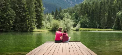 Mother sitting on the dock hugging her son, enjoying the majestic mountain and lake view. Family time and vacation concepts. / Foto: 24k-production