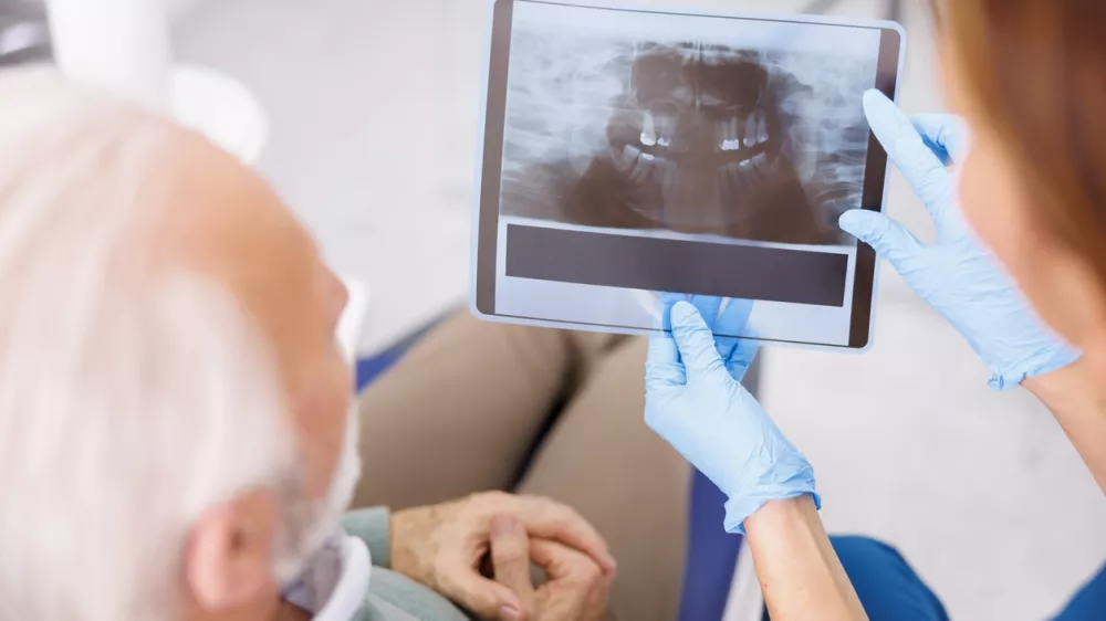 Dentist explaining necessary procedures to patient sitting in dental chair while looking at jaw x-ray at stomatology clinic / Foto: Vladans