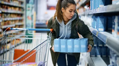 Young woman making food supplies and taking large packet of flour while shopping in grocery store.