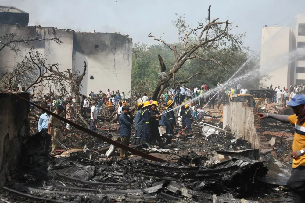 People gather near a damaged building and trees as firefighters work at the site where an Air India plane crashed in Ahmedabad, India, June 12, 2025. REUTERS/Amit Dave