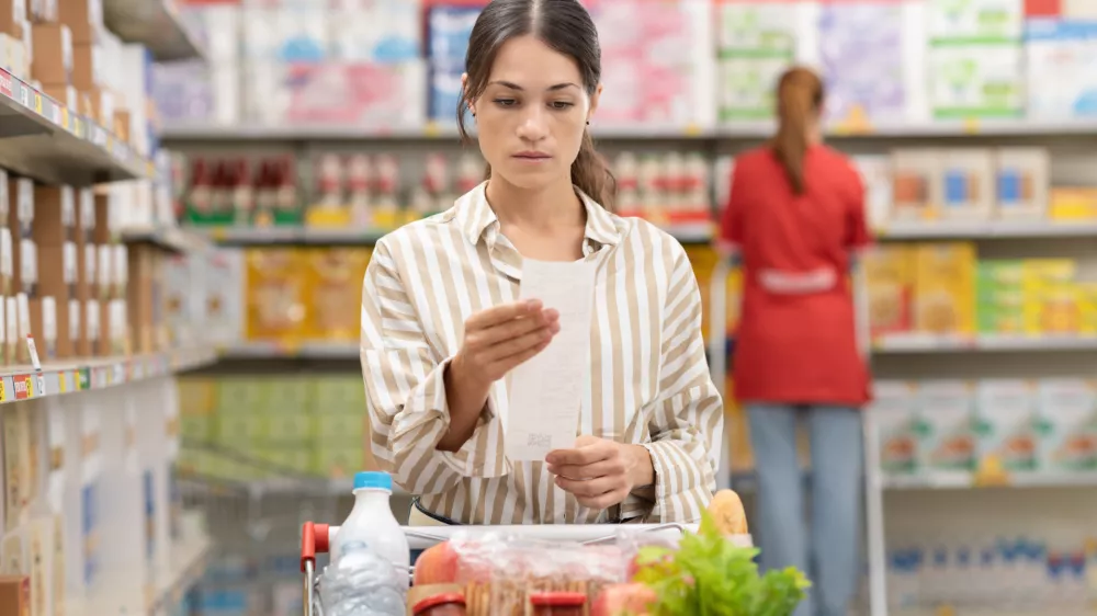 Woman checking a long grocery receipt at the supermarket, grocery shopping and budget concept