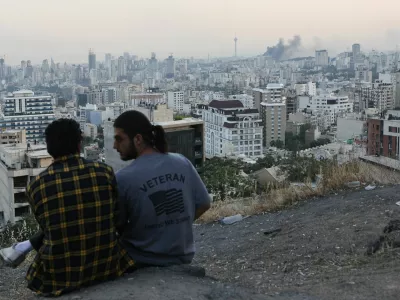 A man wears a U.S. veteran-themed shirt, that reads, "United we stand", as smoke rises in the distance, following an Israeli attack on the IRIB building, the country's state broadcaster, in Tehran, Iran, June 16, 2025. Majid Asgaripour/WANA (West Asia News Agency) via REUTERS  ATTENTION EDITORS - THIS PICTURE WAS PROVIDED BY A THIRD PARTY. TPX IMAGES OF THE DAY.