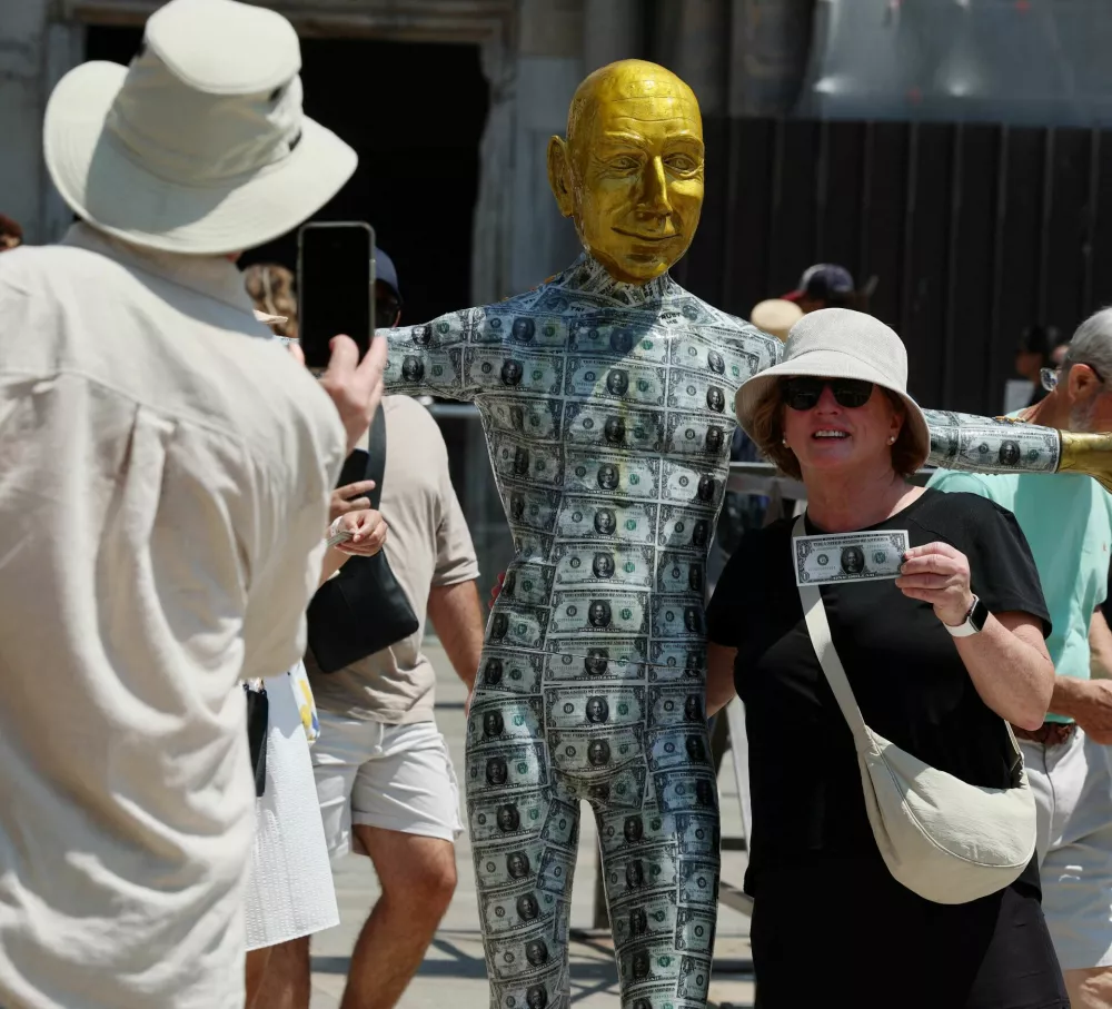 A woman poses holding a fake dollar bill next to a mannequin depicting Amazon Founder Jeff Bezos covered in fake dollar bills installed at St. Mark's Square as part of a parody stunt by art collective Konn Artiss, ahead of the anticipated wedding of Bezos and journalist Lauren Sanchez in Venice, Italy, June 24, 2025. Click News/Handout via REUTERS  THIS IMAGE HAS BEEN SUPPLIED BY A THIRD PARTY. NO RESALES. NO ARCHIVES. MANDATORY CREDIT.