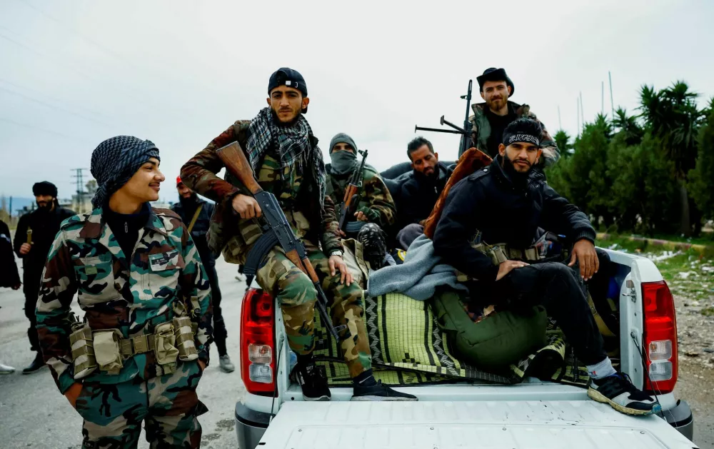 Syrian security forces sit in a pick-up truck on the Latakia-Jableh highway in western Syria, on March 21, 2025. A Reuters investigation found that thousands of forces carried out a wave of deadly attacks on Alawite villages in the region, leaving nearly 1,500 dead from March 7-9, 2025. REUTERS/Stringer  To match Special Report SYRIA-SECURITY/COASTAL-KILLINGS
