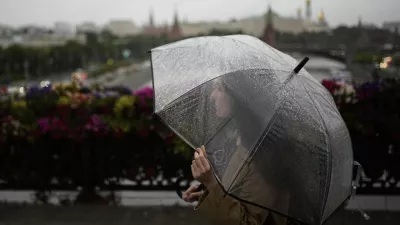 A woman crosses the Patriarshy footbridge holding a transparent umbrella on a rainy day in Moscow, Russia, Monday, June 30, 2025, with the Kremlin in the background. (AP Photo/Pavel Bednyakov)