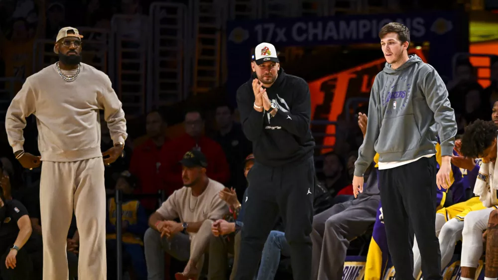 Mar 20, 2025; Los Angeles, California, USA; Los Angeles Lakers forward LeBron James (23), guard Luka Doncic (77), and guard Austin Reaves (15) on the sidelines against the Milwaukee Bucks during the first half at Crypto.com Arena. Mandatory Credit: Jonathan Hui-Imagn Images