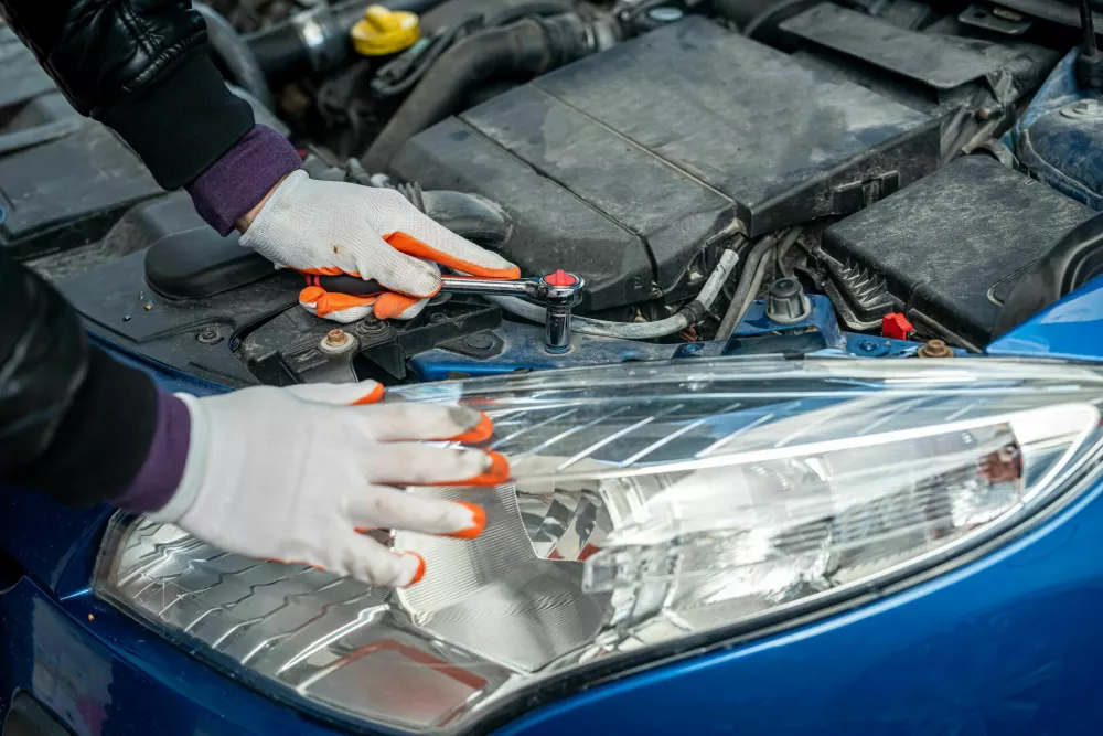 a man in gloves looks under the hood of an open car for a breakdown. Concept of owner and car breakdown