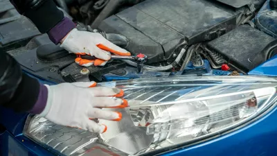 a man in gloves looks under the hood of an open car for a breakdown. Concept of owner and car breakdown