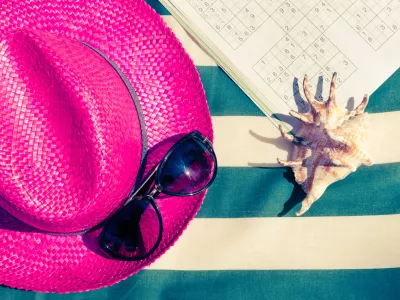 Colorful holiday background with pink straw beach hat with sunglasses and sudoku on striped sunbed. Summer vacation beach leisure activity under the sunlight concept. Flat lay. Top view. Copy space. / Foto: Nellisyr