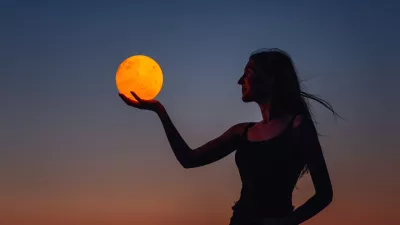 A young woman holds the full moon in her hands against the backdrop of a red sunset. Millennial blogger leads social media. Girl silhouette portrait. Astrology, Waxing Crescent. Copy space / Foto: Julia Pavaliuk